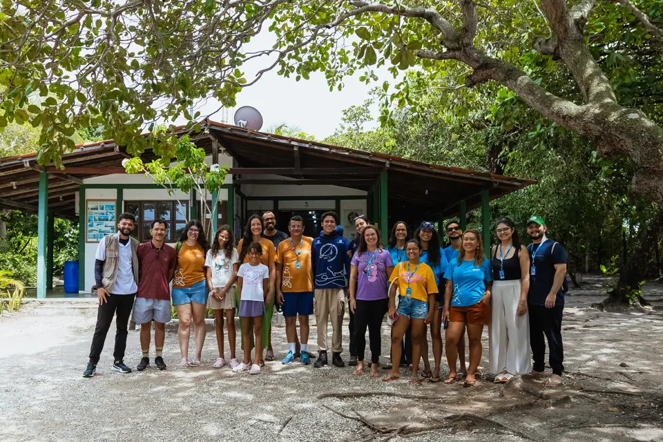 Equipe e moradores reunidos em frente a uma sede comunitária entre árvores